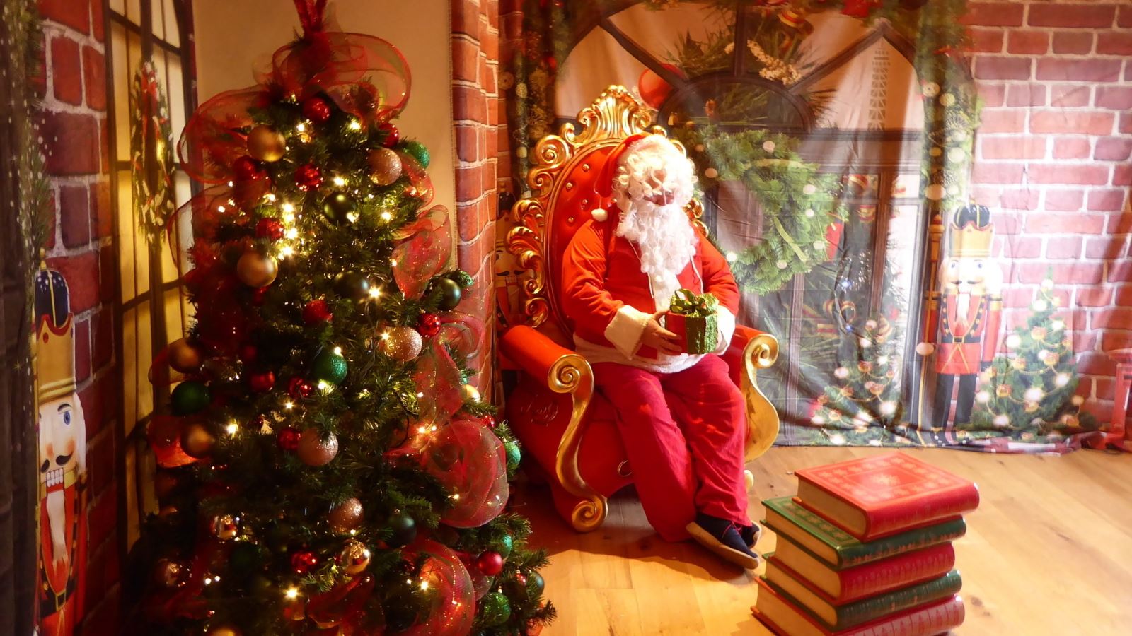 Santa sat next to a Christmas tree holding a present